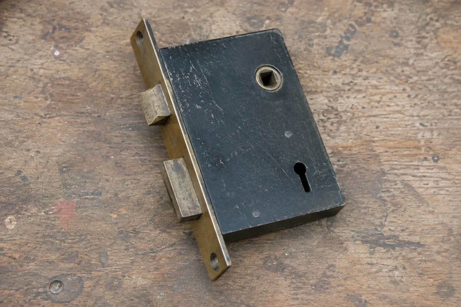 Closed mortise lock case with spindle opening, keyhole, latch and deadbolt on a wooden workbench. — Vintage Mortise Lock Service, Woolwich
