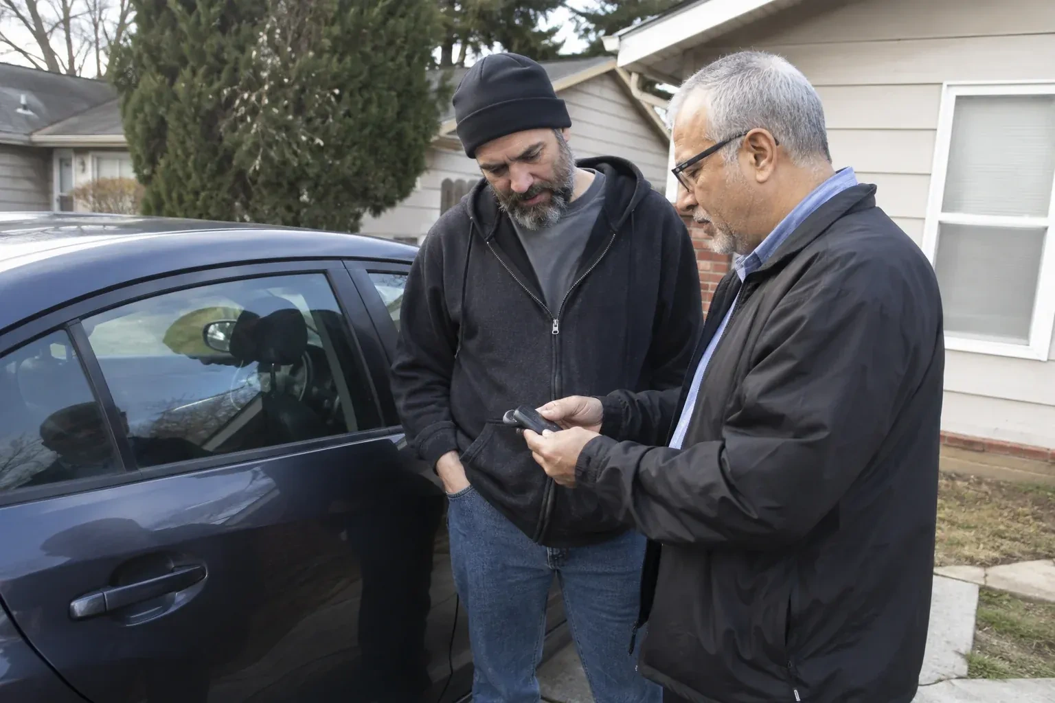 Two adults discussing a key fob beside a parked car. — Car Lockout Service, Floradale